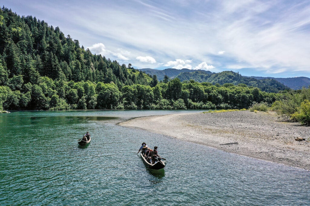 A landscape photo of a river with two canoes full of people.