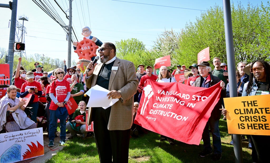 A man speaks into a microphone among a crowd of people holding signs for climate justice.