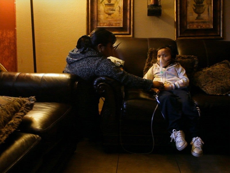 asthma-child_cjb-800 A child, seated in a reclining chair, receives treatment for asthma, as her mother kneels by her side and watches over here.
