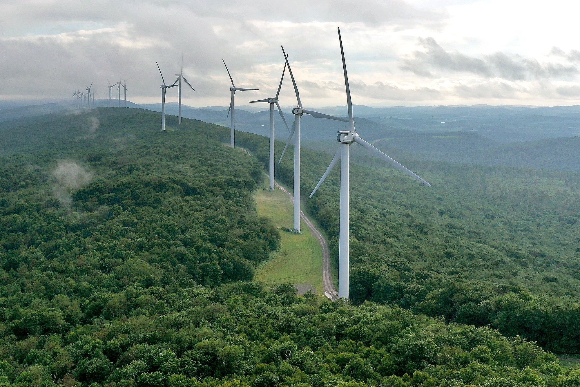 Inflation Reduction Act Boosts Federal Spending On Renewable Energy A long line of wind turbines on a tree covered mountain ridge. In this aerial view, turbines stand in a row along the top of Backbone Mountain on August 22, 2022 in Oakland, Maryland. The 70-megawatt wind farm runs along eight miles of the mountain ridge and consists of 28 Clipper 2.5 MW Liberty Turbines, each one 415-feet tall.